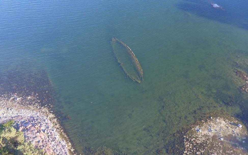 Drönarbild över ett vrak under vattenytan i strandkanten.